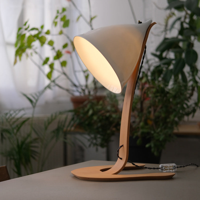 lampe à poser allumée en porcelaine émaillée et bois avec un câble textile torsadé avec des plantes vertes en arrière plan - tsé tsé