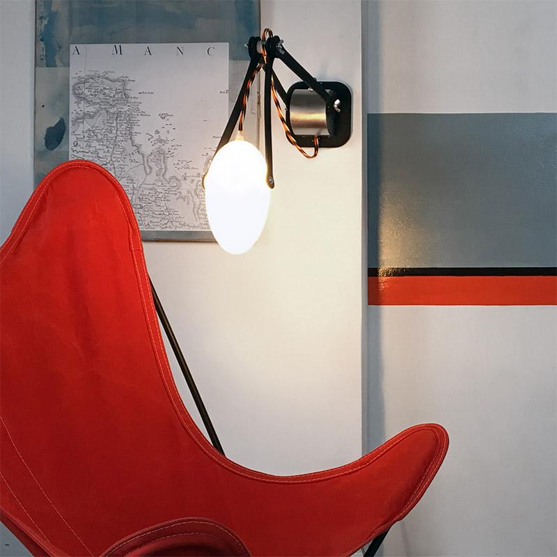 applique articulée en bois noir éclairant un fauteuil papillon rouge - tsé tsé