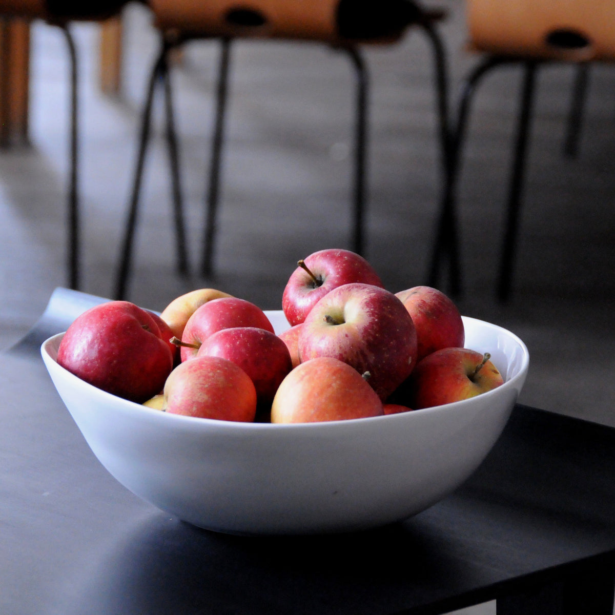 saladier en porcelaine blanche rempli de pommes posé sur une table basse noire - tsé tsé