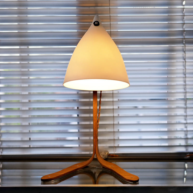 lampe à poser avec des pieds en bois et un cornet en porcelaine translucide, devant un store. Tsé & Tsé