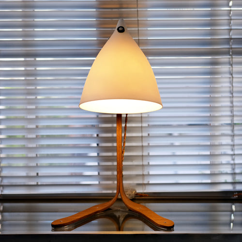 lampe à poser avec des pieds en bois et un cornet en porcelaine translucide, devant un store. Tsé & Tsé