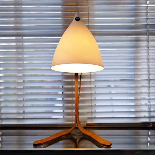 lampe à poser avec des pieds en bois et un cornet en porcelaine translucide, devant un store. Tsé & Tsé