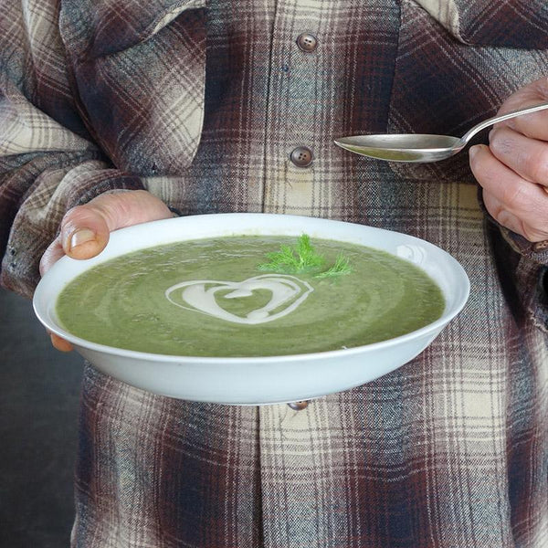 soupe verte dans une assiette creuse blanche tenue en main - tsé tsé