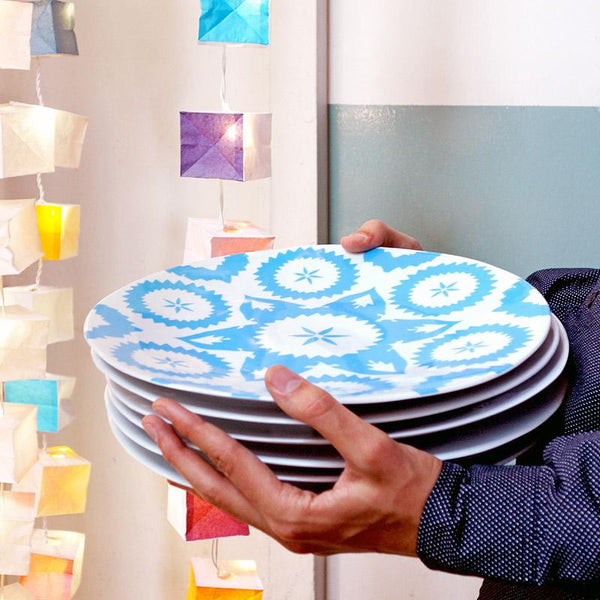 pile de grandes assiettes en porcelaine bleue et blanche à motifs tenue en main et guirlande lumineuse en papier en arrière plan - tsé tsé