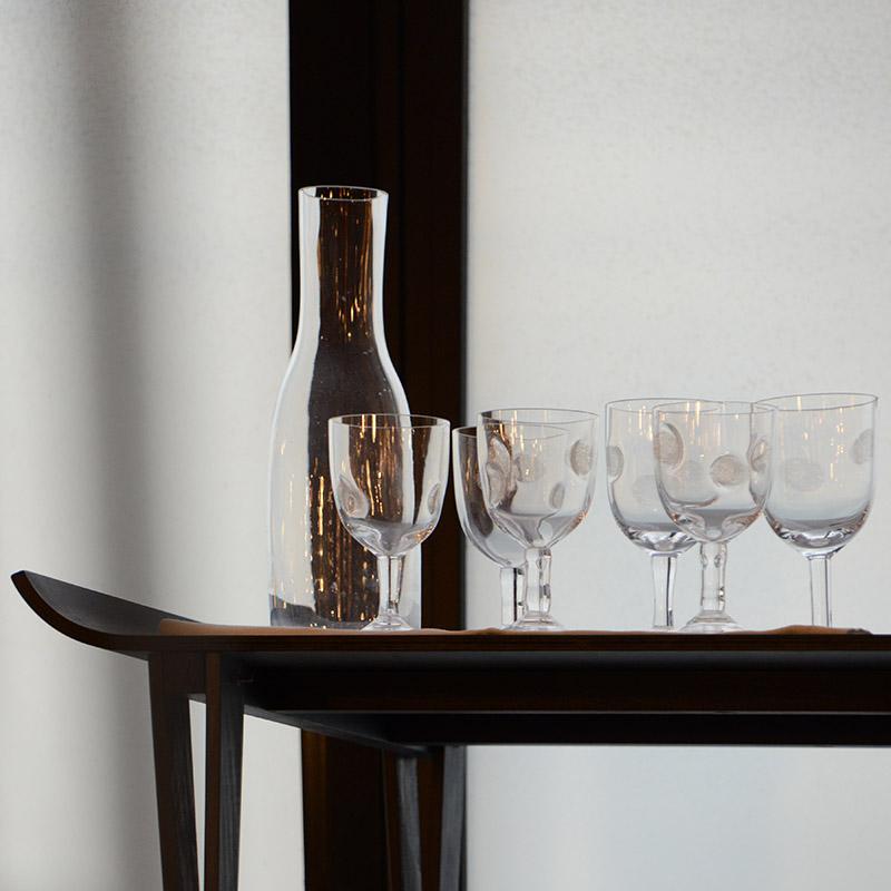 carafe en verre irégulière et verres à pieds incrustés de traces de doigt posés sur une table noire - tsé tsé