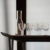 carafe en verre irégulière et verres à pieds incrustés de traces de doigt posés sur une table noire - tsé tsé