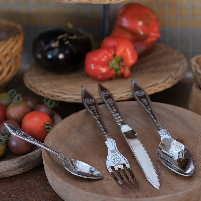 couverts de table en acier poinçonné présentés sur une assiette en bois avec des légumes en fond - tsé tsé