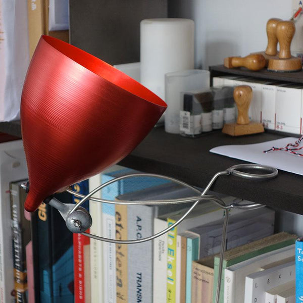 lampe rouge métallisé fixée par une pince à une bibliothèque noire - tsé tsé