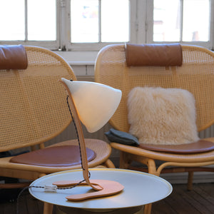 lampe en porcelaine blanche et bois clair posée sur une table basse devant des fauteuils en rotin avec des coussins en cuir - tsé tsé