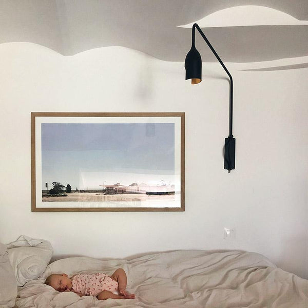 grande lampe pivotante en alu laqué noir fixée au mur au dessus d'un lit dans lequel dort un bébé - tsé tsé