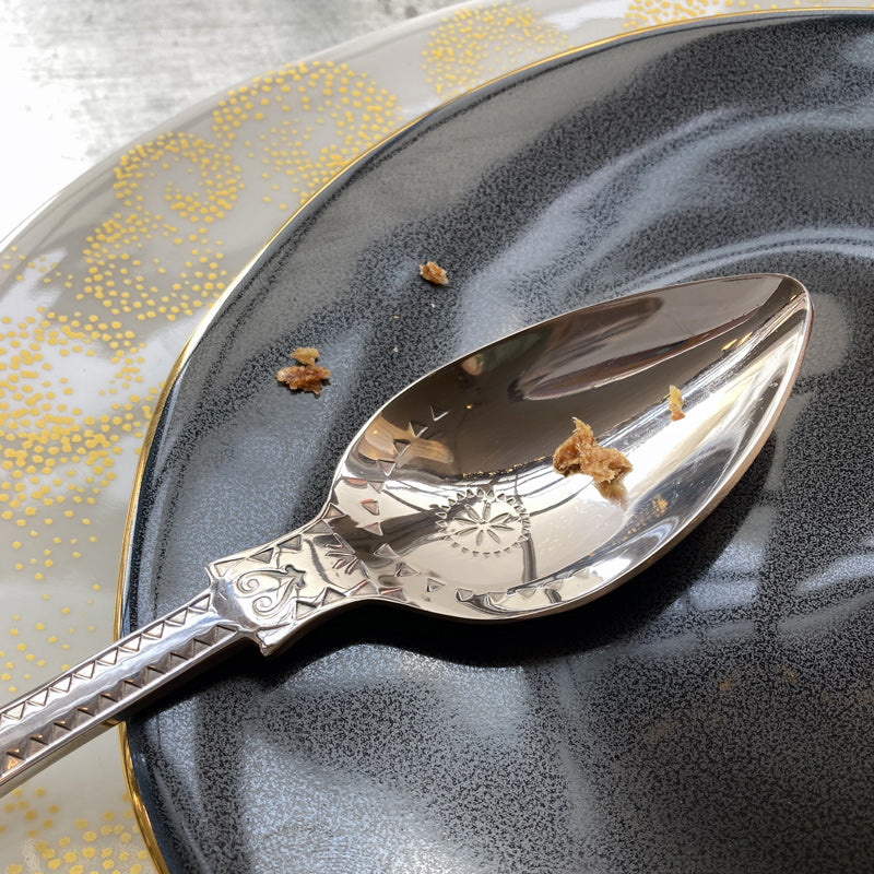 détail cuillère à dessert en inox embouti avec des miettes dans une assiette bleu et or - tsé tsé
