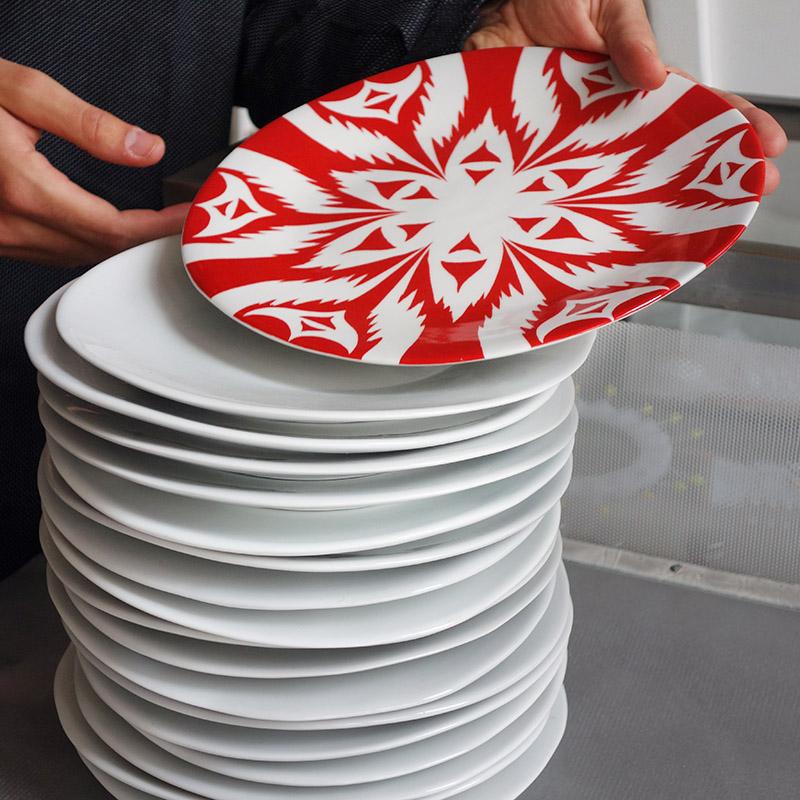 pile d'assiettes blanches en porcelaine, recouverte d'une assiette rouge vermillon au motif graphique - tsé tsé