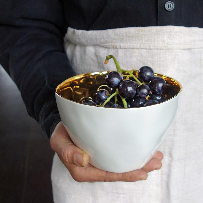 grand bol de forme irrégulière blanc et or rempli de raisin noir et tenu à une main - tsé tsé