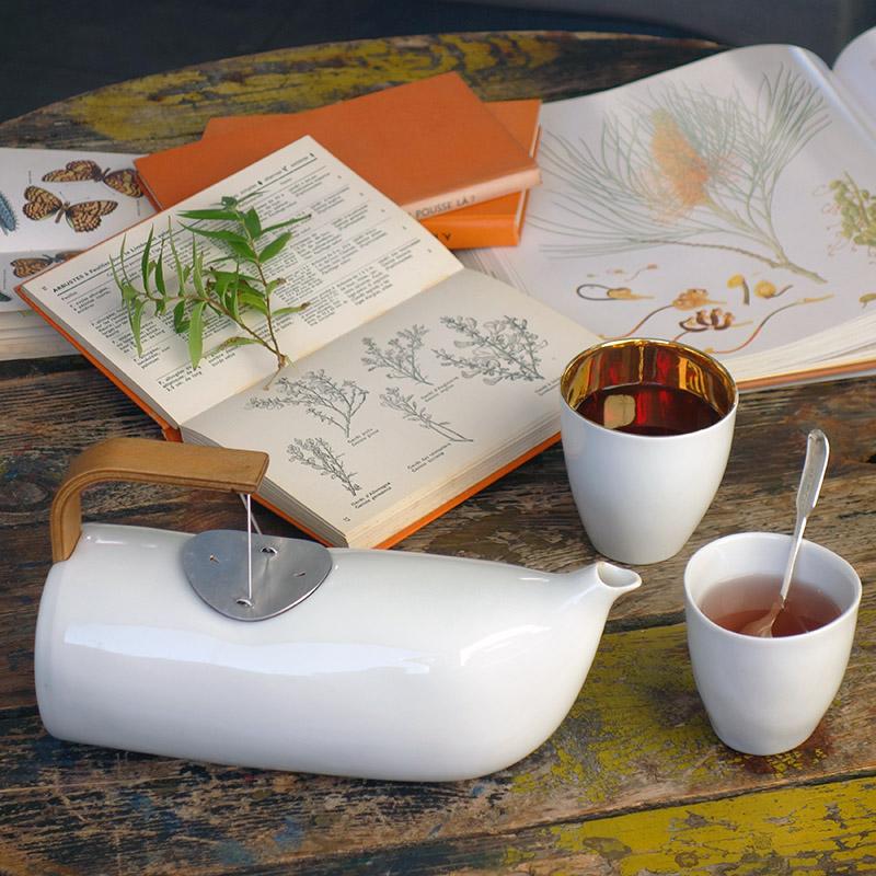 tasse à thé blanche intérieur or sur une table avec une théière et des livres - tsé tsé