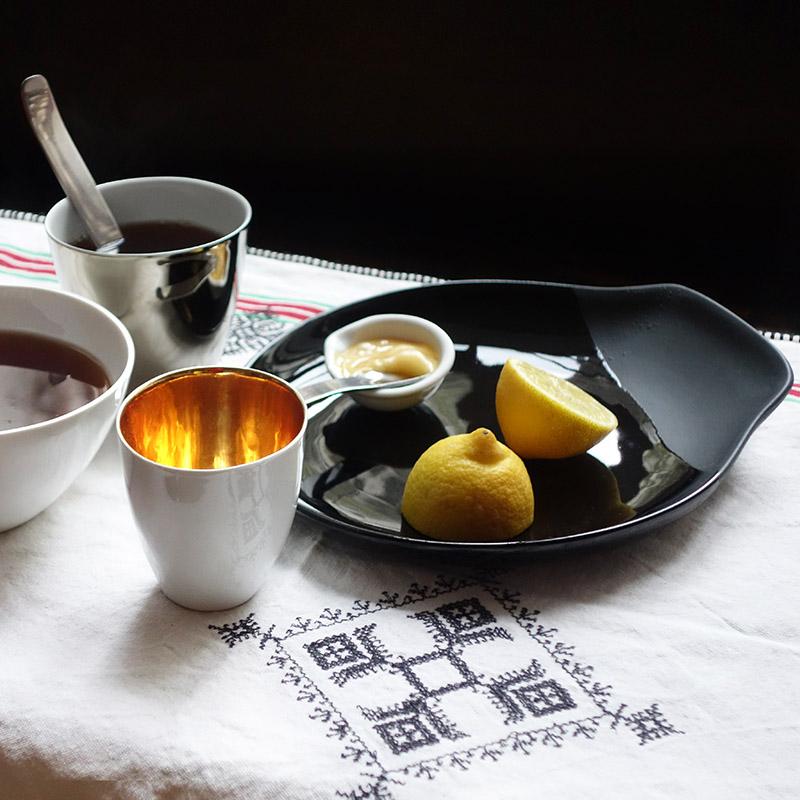 table avec nappe brodée, assiette noire et tasse blanche et dorée - tsé tsé