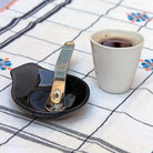 gobelet à expresso blanc et cuillère à café avec le manche ondulé dnas une soucoupe asymétrique noire - tsé tsé