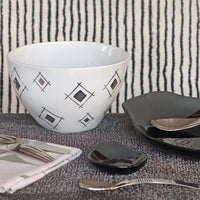 assiettes noires et saladier blanc à motifs argentés effet miroir devant un mur noir et blanc rayé - tsé tsé